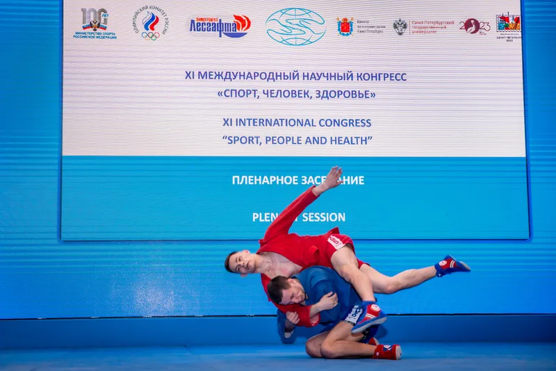 Спортсмены в красной и синей форме демонстрируют приём на сцене XI Международного научного Конгресса «Спорт, Человек, Здоровье»